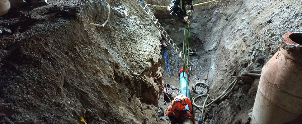 En person arbetar nere i en djup grävd grop för att laga en vattenläcka i Falköping.